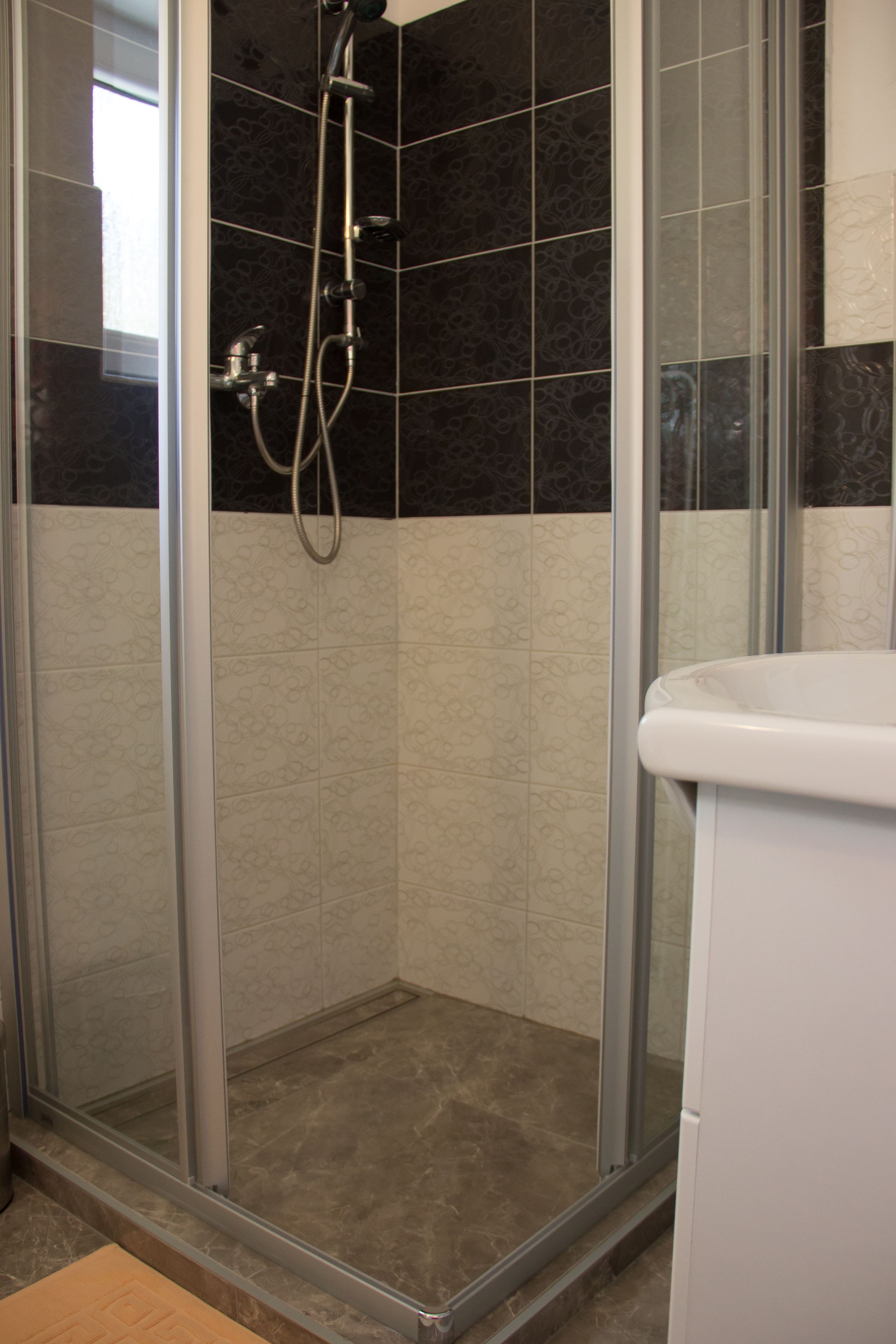 Un área de ducha con puerta de vidrio, un lavamanos blanco y azulejos estampados.