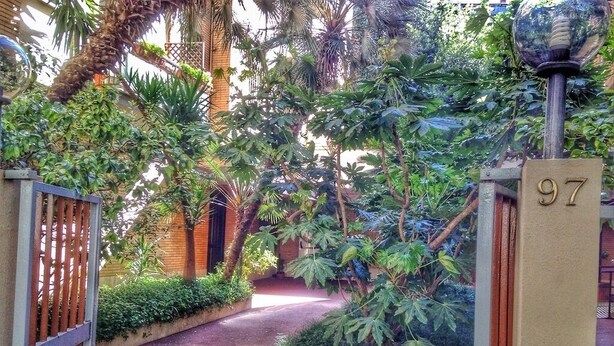Ein verschlossenes Tor mit einer Beschilderung, umgeben von üppiger Vegetation und einem Weg zu einem Gebäude.