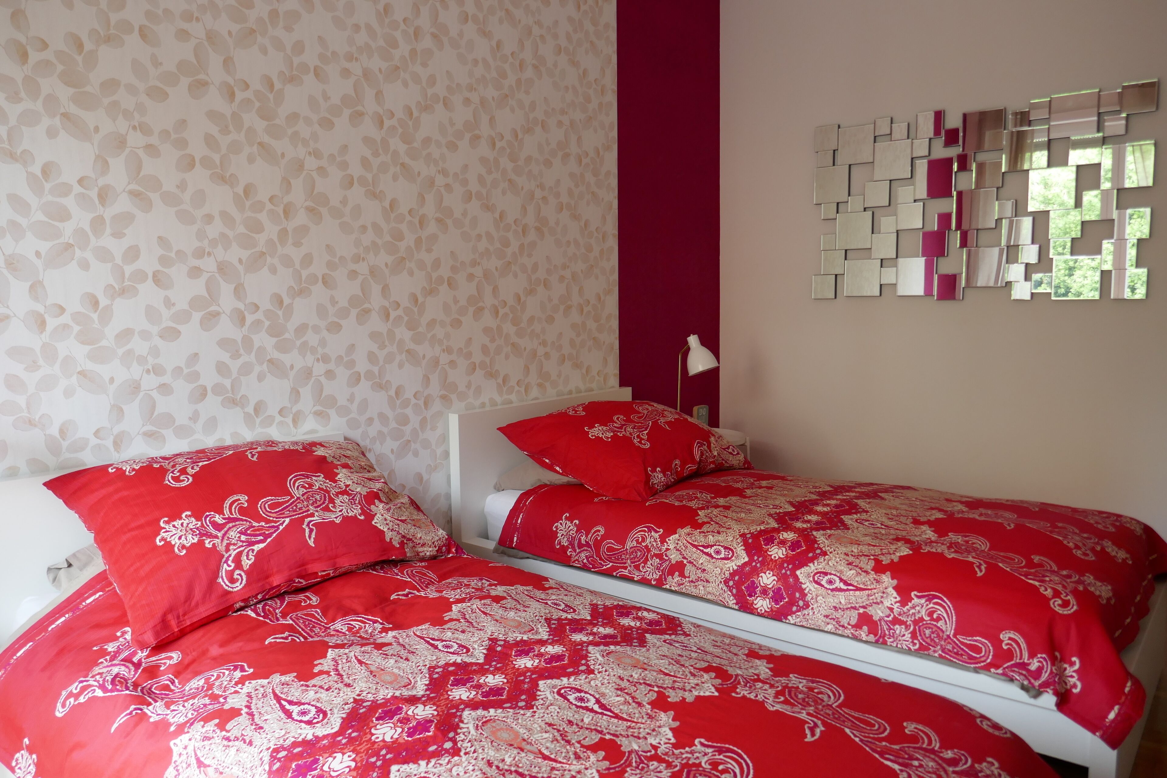 A bedroom with two beds, a patterned wall, and a mirror with geometric shapes.