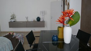 Un espace repas moderne avec une table en verre, des chaises noires, un canapé et un meuble blanc agrémenté d’objets décoratifs.