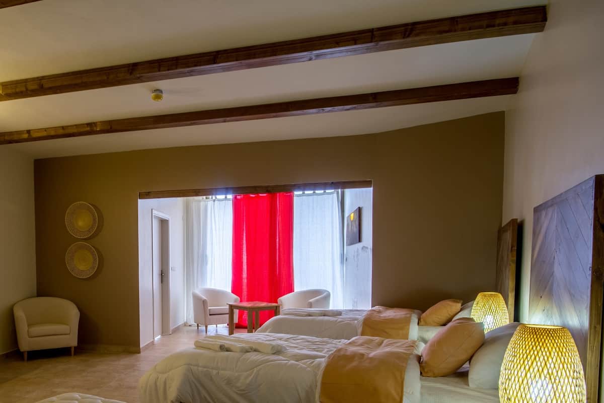 A hotel room with a bed, two chairs, a small table, and a red curtain.