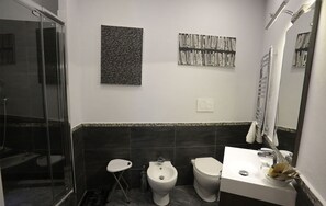 A modern bathroom with a glass shower enclosure, a bidet, a toilet, and a sink with a mirror. - Attico Volta B&B (Foggia)