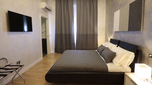 A bedroom with a bed, a flat-screen TV mounted on the wall, a window with curtains, and a bedside table with a lamp. - Attico Volta B&B (Foggia)
