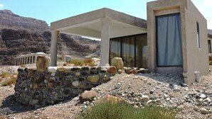 A modern building with a stone foundation, a covered patio area, and a glass door.