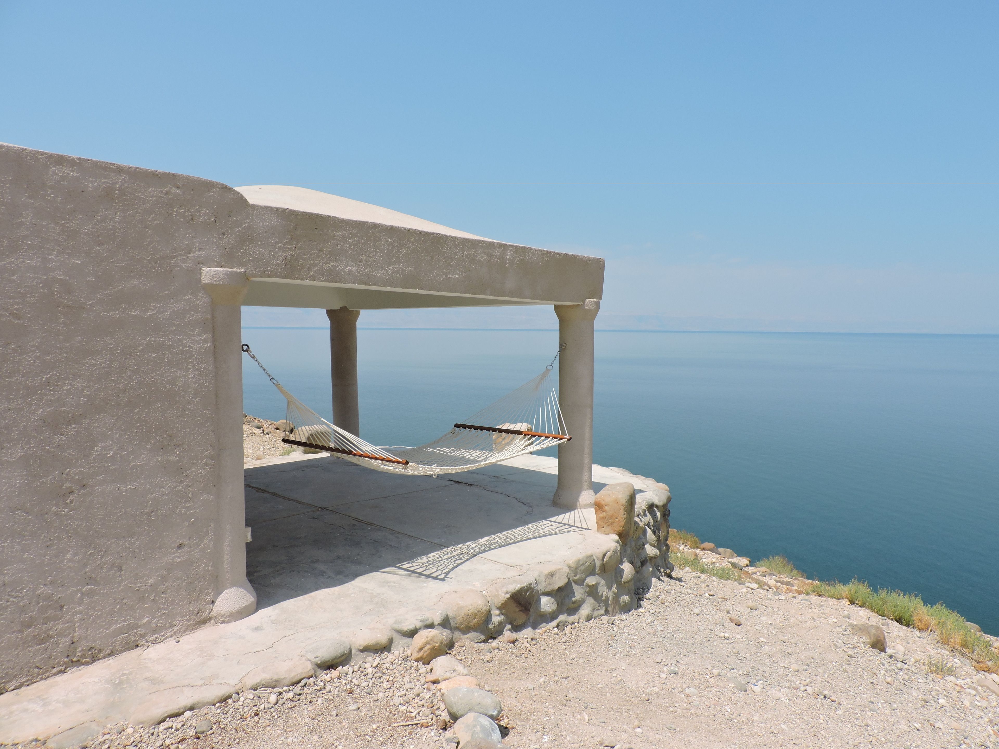 Estructura de concreto con una hamaca bajo un área sombreada con vista al mar tranquilo.