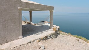 A concrete structure with a hammock under a shaded area overlooking a calm sea.