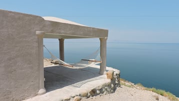 Estructura de concreto con una hamaca bajo un área sombreada con vista al mar tranquilo.