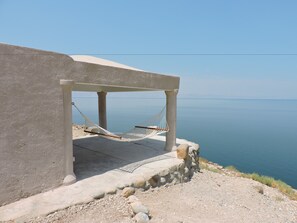 A concrete structure with a hammock under a shaded area overlooking a calm sea.