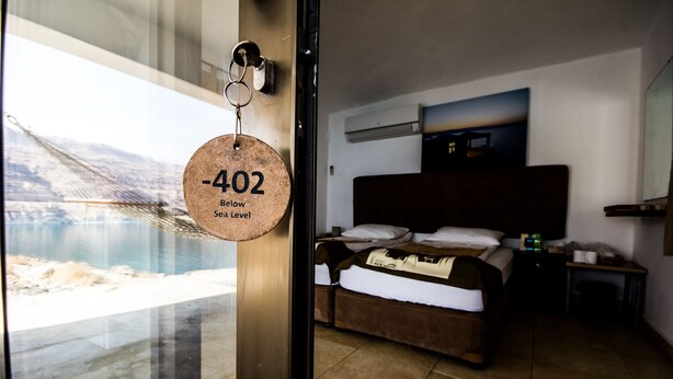 A hotel room with a bed, a nightstand, and a view of a body of water through a window.
