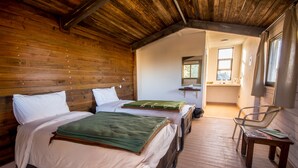A cozy cabin-style room with two beds, a wooden floor, a small table, and a chair. - Ajloun cabins (Ajloun)