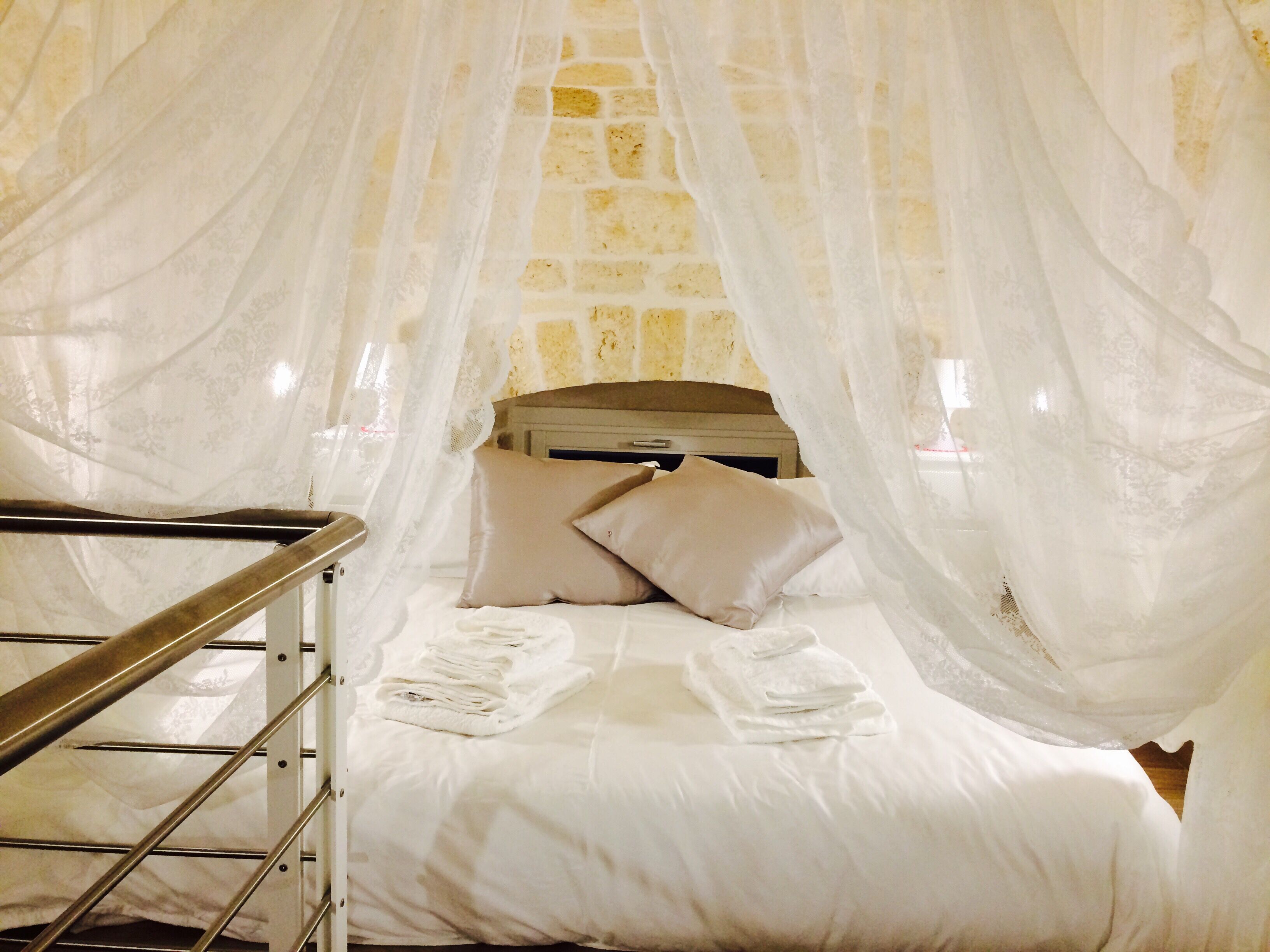 Un dormitorio con cama, ropa de cama blanca, cabecero de madera y pared de ladrillo.