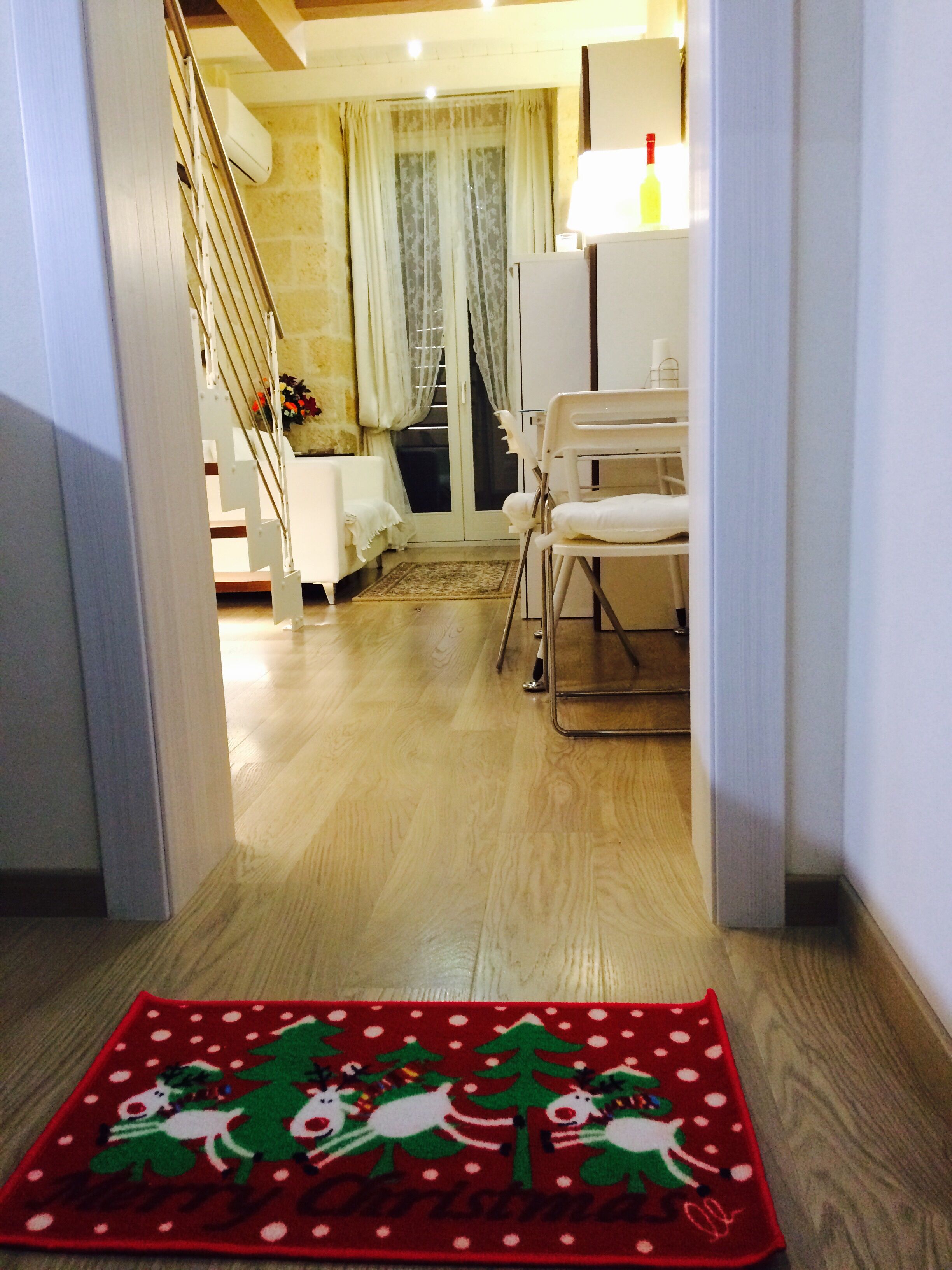 A hallway with a wooden floor leading to a room with a white chair and a small table.