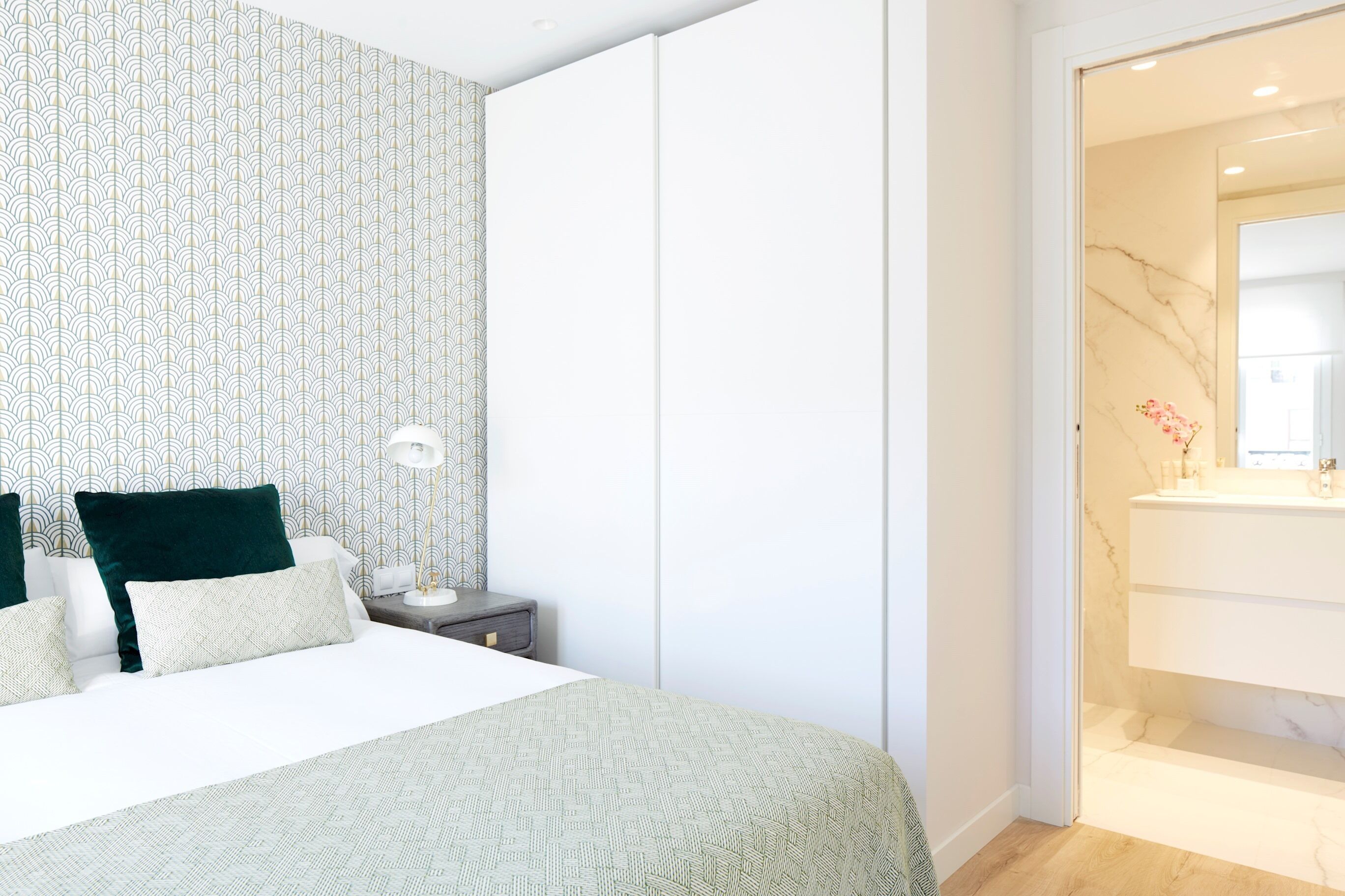 A modern bedroom with a bed, nightstand, and a bathroom visible through an open door.