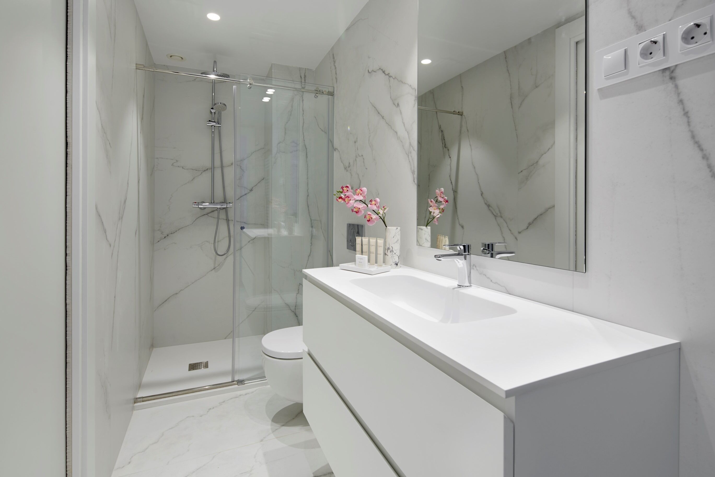 Une salle de bain moderne avec une douche à parois de verre, un lavabo blanc et un pare-baignoire en marbre.