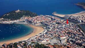 Vista aérea de una ciudad costera con una colina destacada, una playa y un puente que conecta dos zonas.