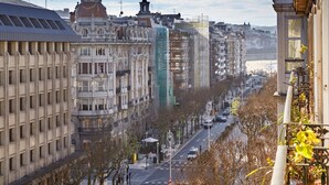 Una calle urbana con edificios históricos, un moderno edificio de cristal y vistas al mar.