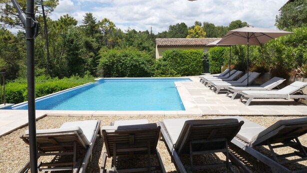 A swimming pool with lounge chairs and umbrellas, surrounded by greenery and a tiled roof structure. - MONTAUROUX 30MN OF CANNES APARTMENT CONDITIONING TERRACE GARDEN PRIVATE POOL (Montauroux)