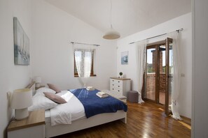 A bedroom with a bed, bedside table, lamp, window, and a view of the outside.