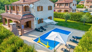 A two-story house with a swimming pool, outdoor furniture, and a garden.