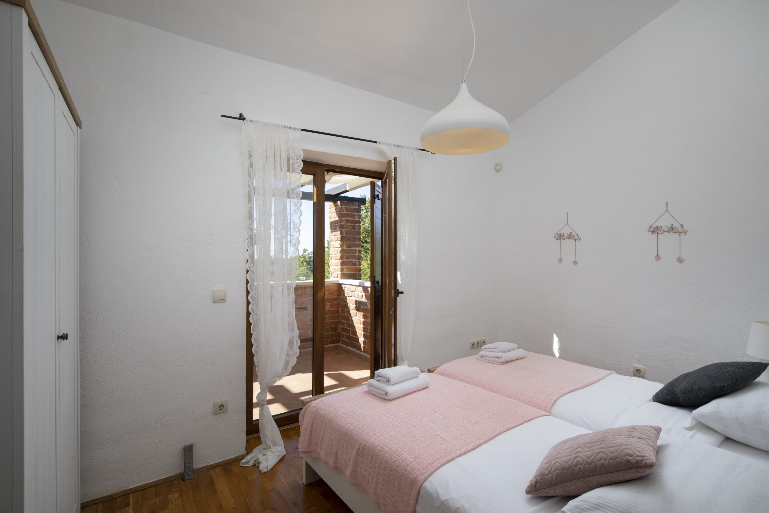 A bedroom with a bed, a hanging light, a window with curtains, and a view of the outside.
