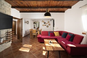 Een gezellige woonkamer met een rode bank, een houten salontafel en een eethoek met een houten tafel en stoelen.