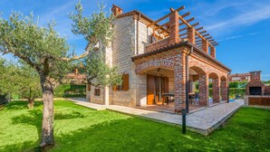 A stone house with a patio, a pergola, and a swimming pool in the background.