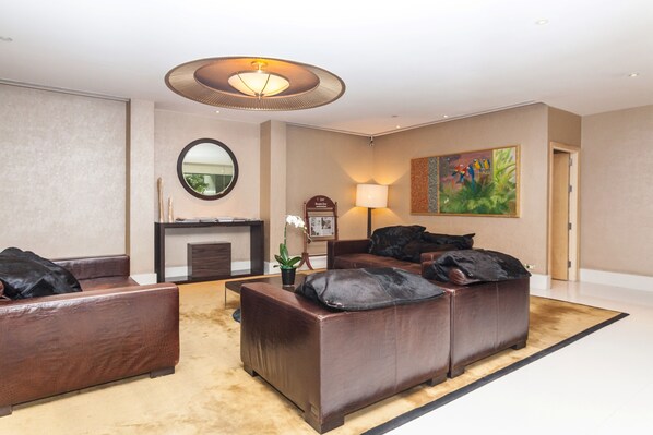 A modern living room with a fireplace, leather sofas, a round mirror, and a painting on the wall. - Serviced 2 Bed SCENIC SKY VILLAS with Pool and BTS (Bangkok)