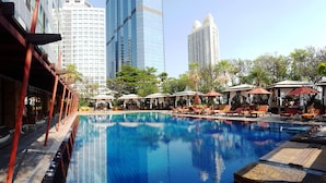 Ein Swimmingpool mit Liegestühlen und Sonnenschirmen, umgeben von Bäumen und Gebäuden.