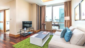 Ein modernes Hotelzimmer mit Flachbildfernseher, einem Glastisch, einer blauen Sitzecke und einem großen Fenster mit Vorhängen.