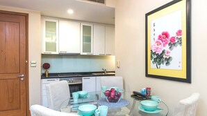 Una cocina moderna con armarios blancos, una mesa de comedor de vidrio y cuencos color turquesa, y una obra de arte enmarcada con flores rosadas.