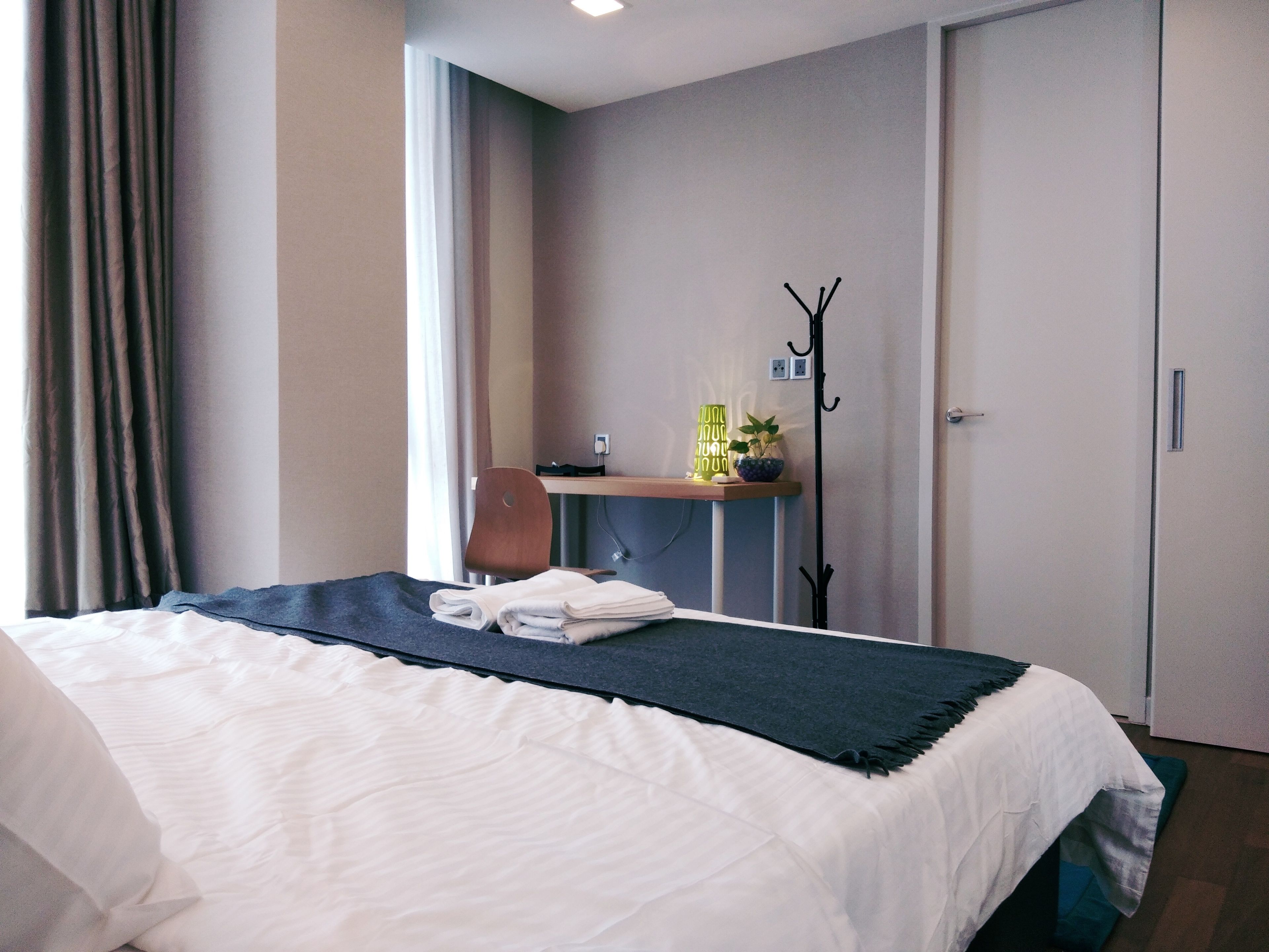 A hotel room with a bed, a desk with a chair, a coat rack, and a wardrobe.