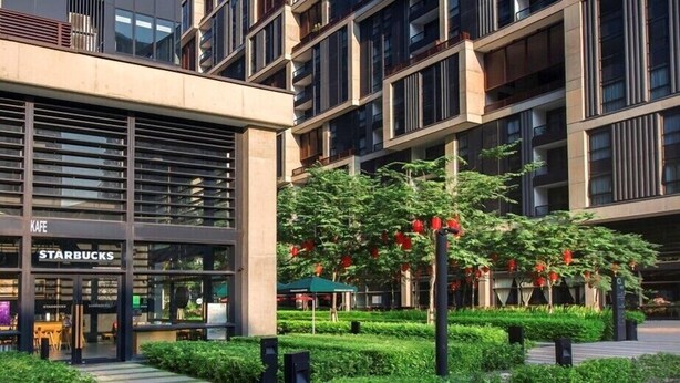 Un bâtiment moderne abritant un Starbucks au rez-de-chaussée, entouré d’un espace vert bien entretenu et sous un ciel dégagé.