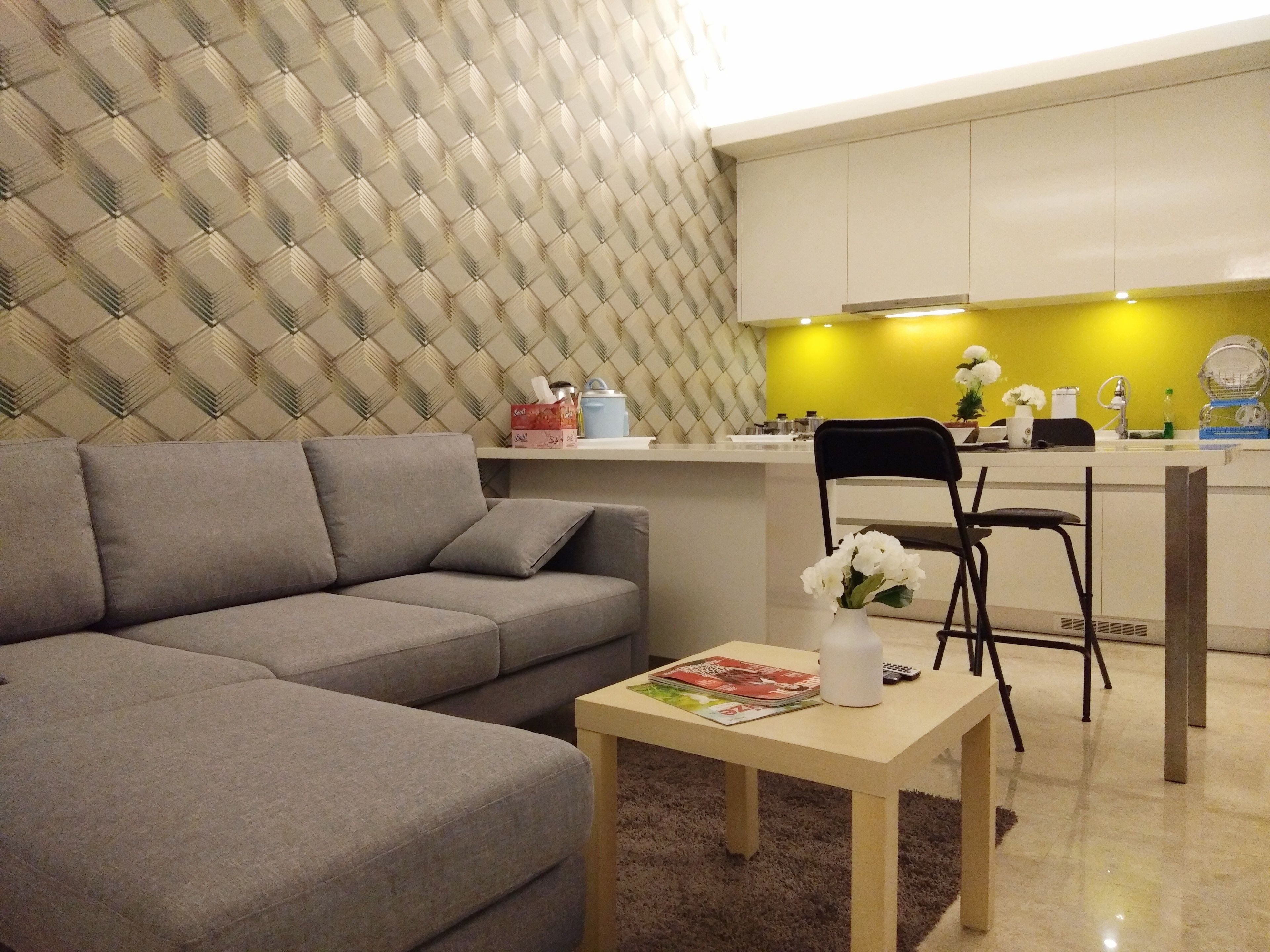 A modern living room with a grey sofa, a wooden coffee table with magazines, and a small white vase with flowers.