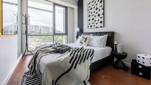 Une chambre à coucher moderne avec une grande fenêtre, un lit doté d’une tête de lit noire, une table de chevet avec une lampe et une œuvre d’art accrochée au mur.