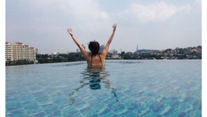 Une personne dans une piscine, les bras levés, avec des bâtiments en arrière-plan.