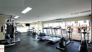 Un gimnasio con cintas de correr, máquinas de pesas y un amplio ventanal con vistas a edificios.