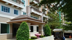 Un hotel de varios pisos con entrada cubierta, un jardín ajardinado con una gran jardinera y un teléfono público.
