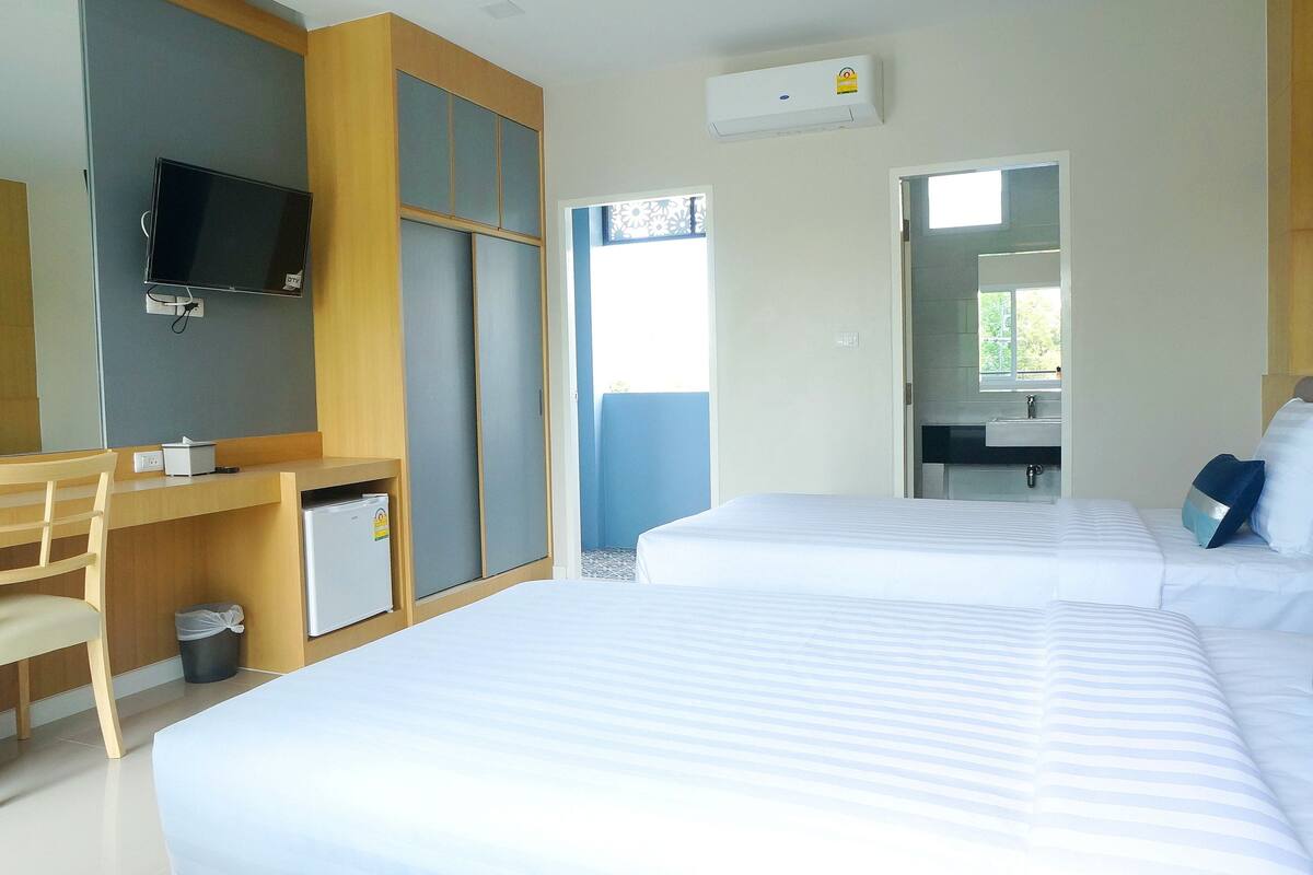 Ein Hotelzimmer mit zwei Betten, einem Schreibtisch mit Stuhl, einem Fernseher und einem kleinen Kühlschrank.