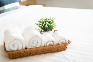 Una cama ordenada con sábanas blancas y una pequeña planta en maceta.