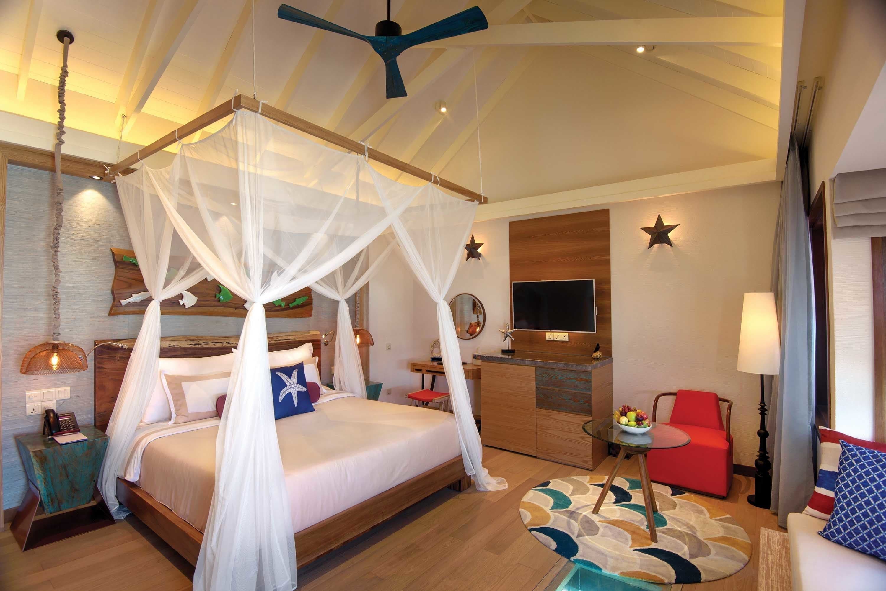 Un dormitorio amplio con cama con dosel, un escritorio, un sillón rojo y un televisor.