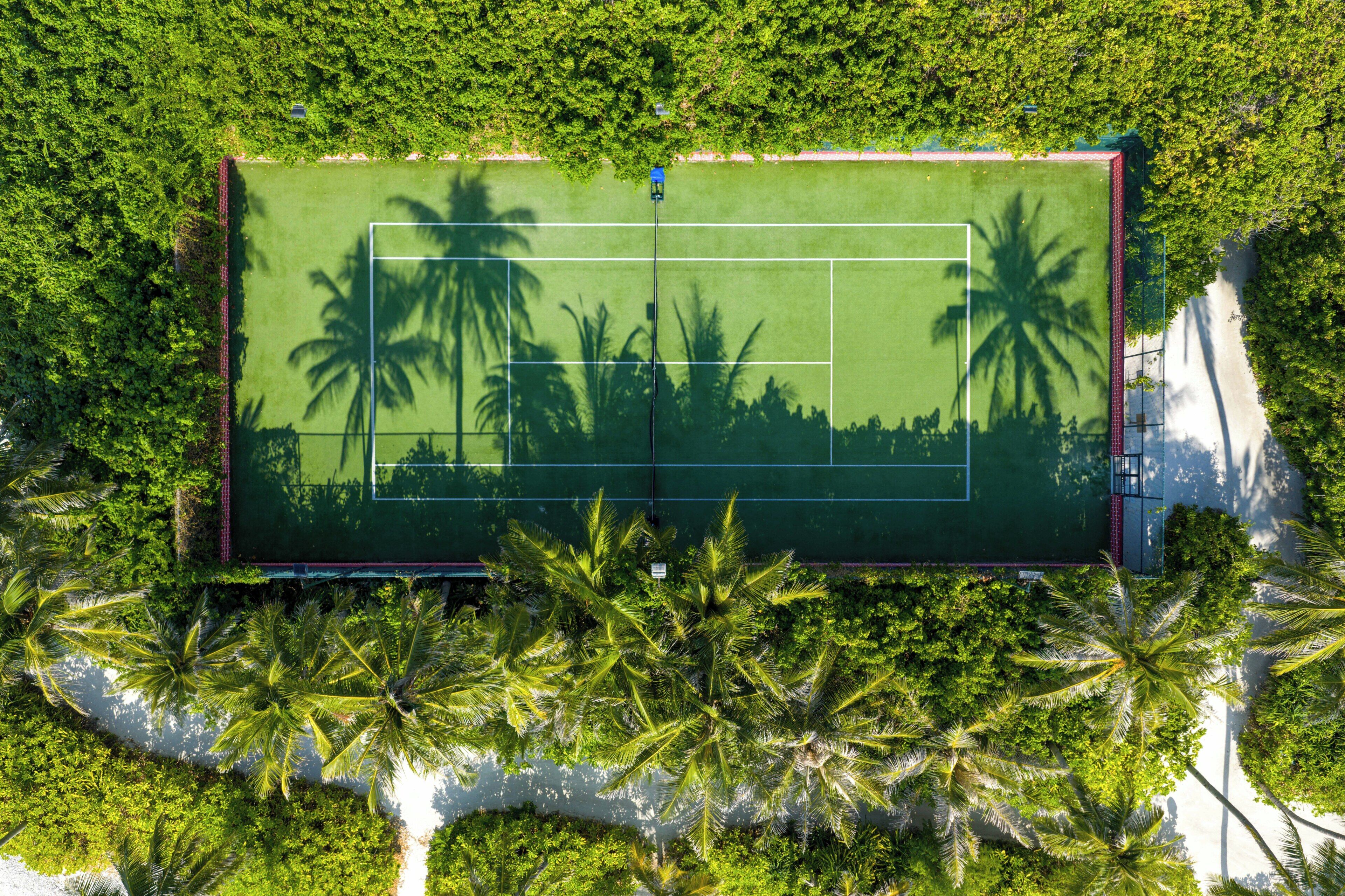 Vista aerea di un campo da tennis circondato da vegetazione lussureggiante e palme.