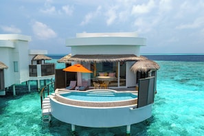 A resort overwater bungalow with a pool, lounge chairs, and a thatched roof.