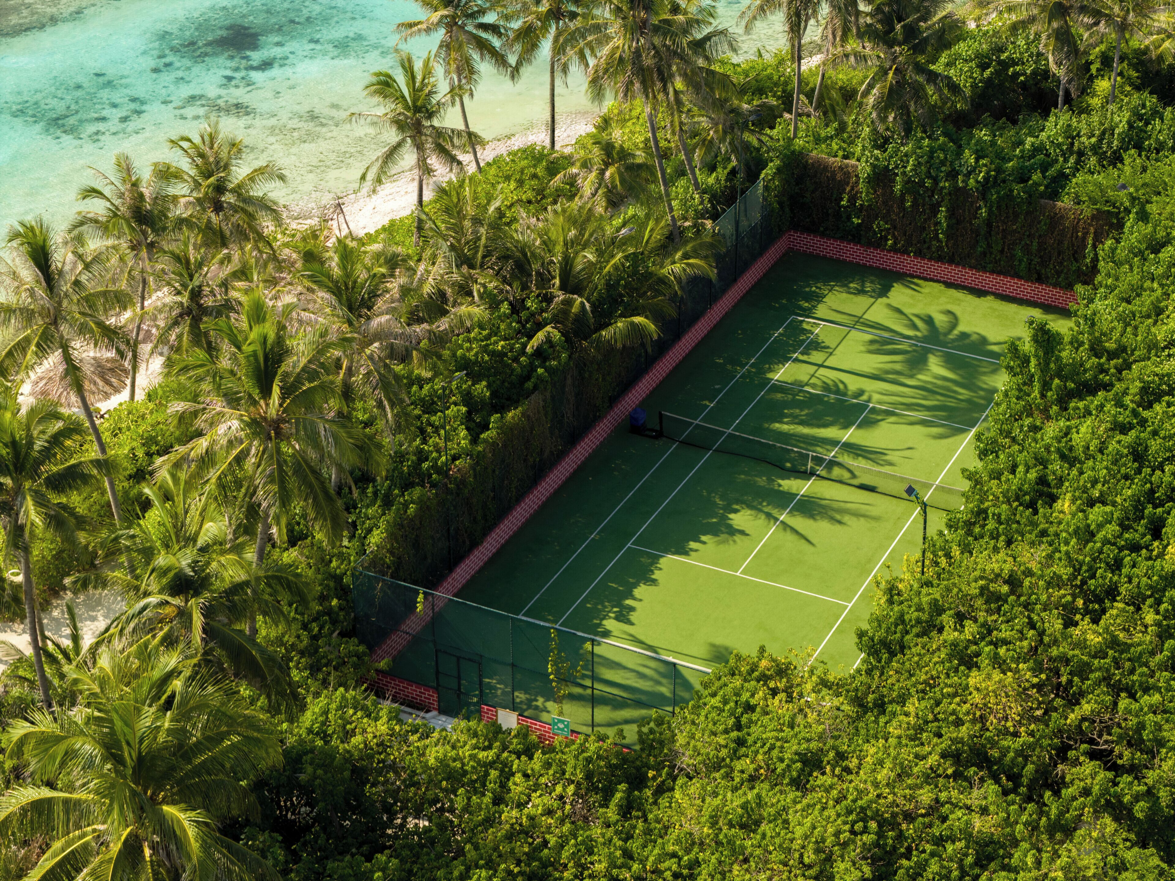 Ilmakuva tenniskentästä, jonka ympärillä on vehreää kasvillisuutta ja ranta.
