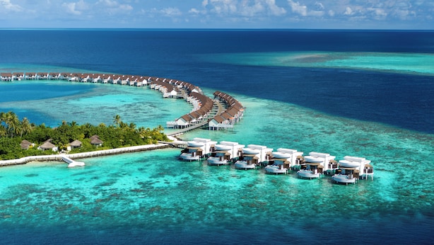Conjunto de bungalows sobre el agua con una disposición curva, unidos por pasarelas, rodeado de aguas turquesas cristalinas.