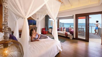 Un dormitorio con cama con dosel, televisión, sofá y vista al océano.