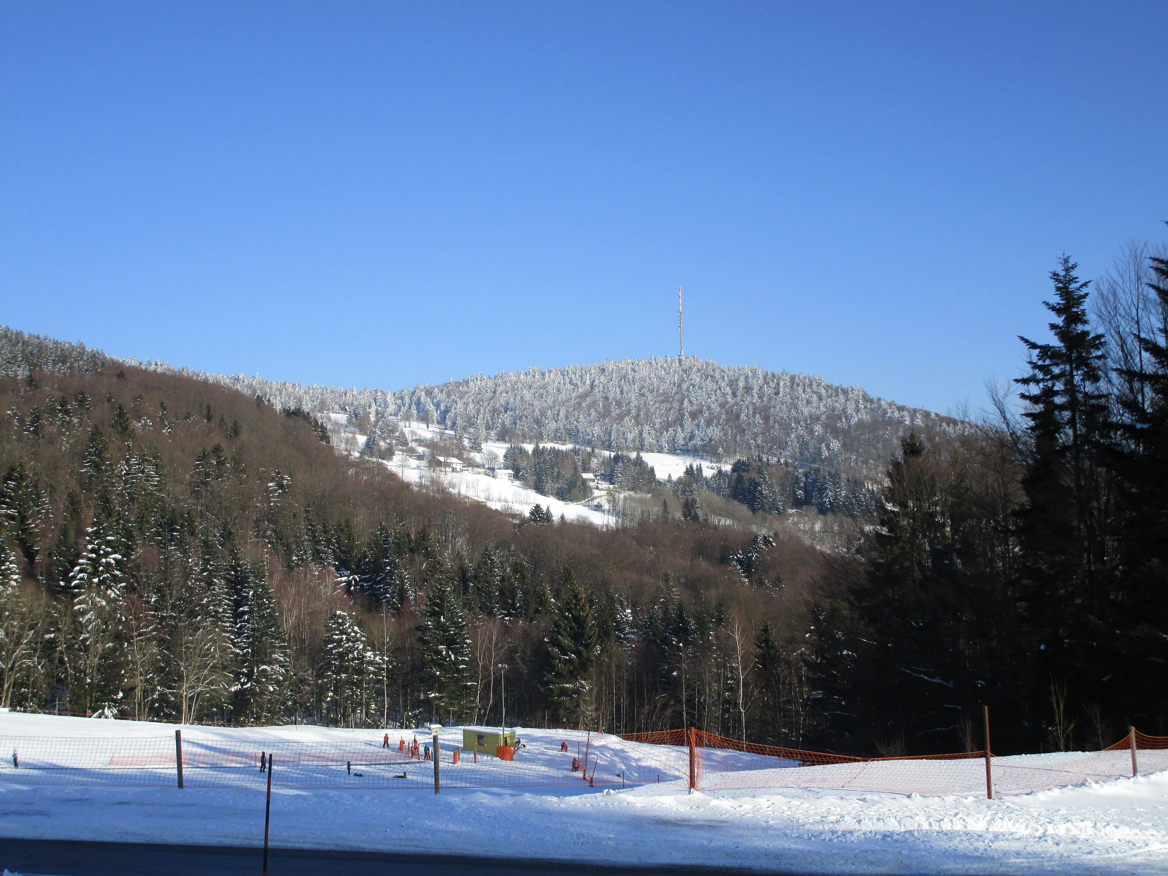 A snow-covered landscape with a ski resort, including a ski lift, trees, and a mountain backdrop.