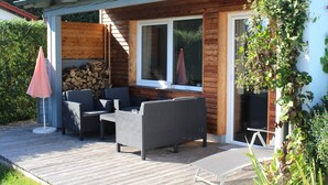 An outdoor patio with wicker furniture, a wooden deck, and a stone wall. - Newly renovated holiday home in the Bavarian Forest (Schöfweg)