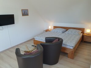 Ein Schlafzimmer mit einem Bett, zwei Nachttischen mit Lampen, einem Fernseher an der Wand und einem kleinen Tisch mit einem Stuhl.