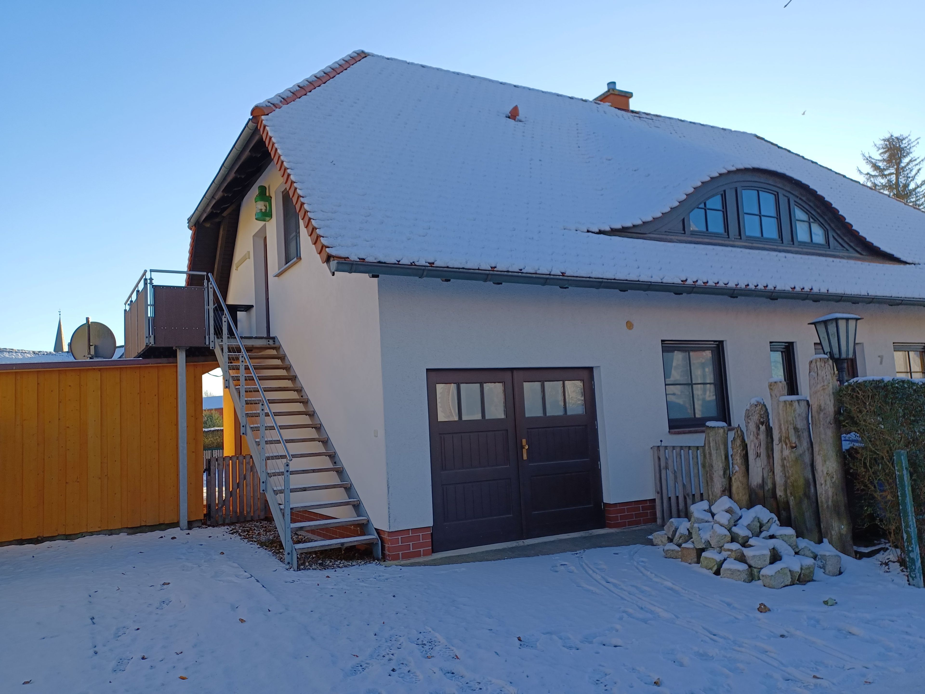 A two-story house with a snow-covered roof, a wooden staircase, and a garage.