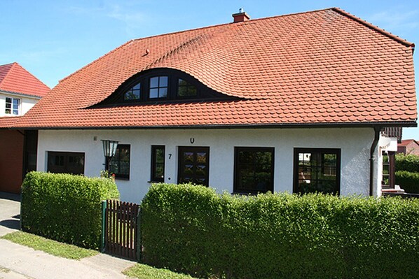 A two-story house with a red-tiled roof, white exterior walls, and a small front porch.
